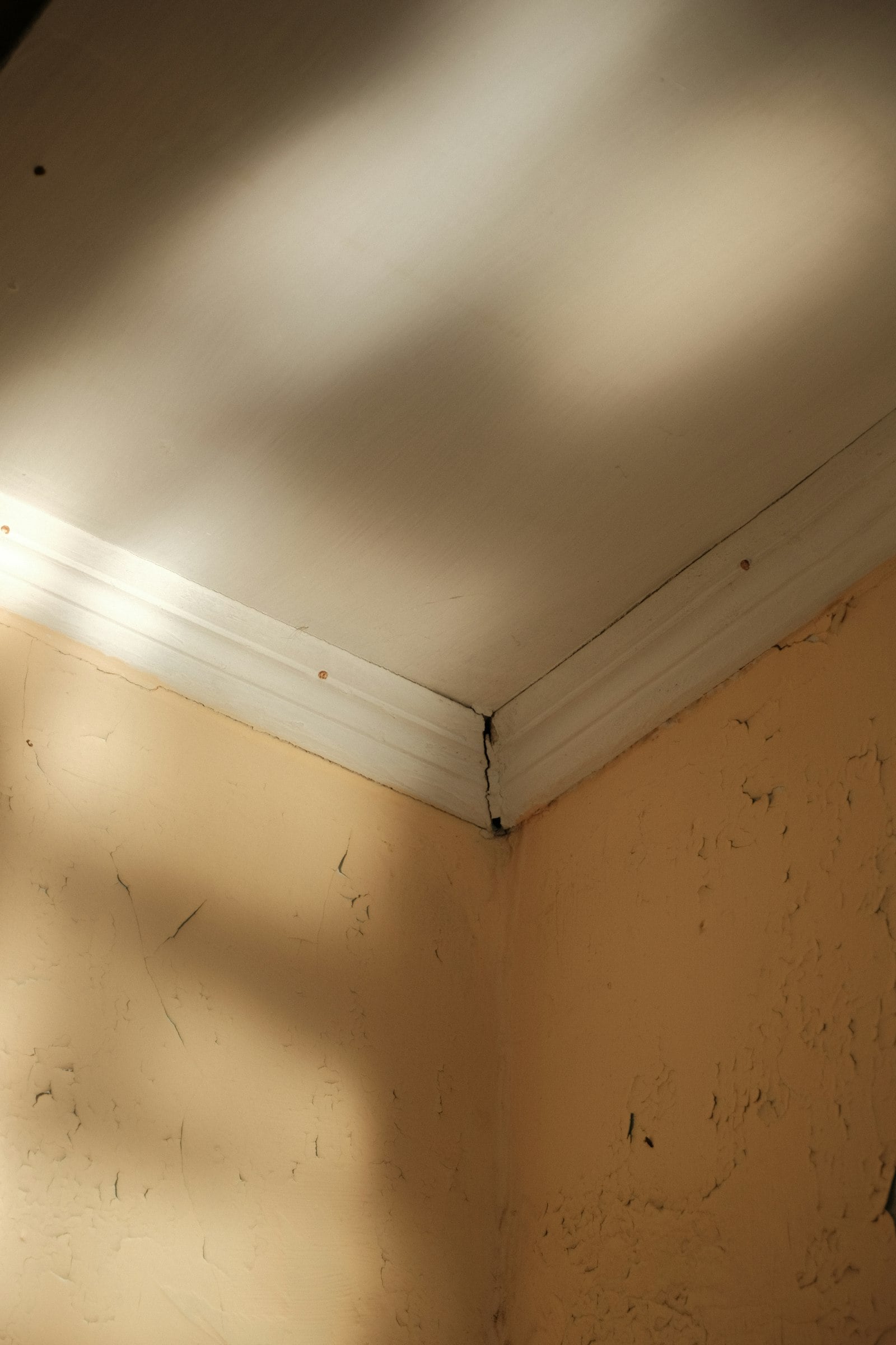 Corner of an empty room lit through a ceiling opening